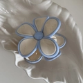 Detailopname van de crème bloem haarklem met blauwe randen op een schelptray - Crèmewit Bloemblad Blauwe Rand