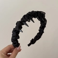 Cerchietto punk nero plissettato con borchie lucide mostrato su uno sfondo beige - Cerchietto Nero Avvolto Con Denti