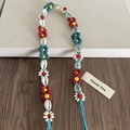 Détail d'un accessoire tressé bohème avec fleurs en perles colorées et coquillages naturels - Fleurs Rouge Vert Coquillage