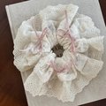 Detailaufnahme von cremefarbenem Spitzen-Haargummi mit rosa Schleifen auf Leinenbuch - Creme Mit Rosa Schleife