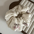 Nahaufnahme von cremefarbenem Spitzen-Scrunchie mit Kirsstickerei und Webetikett - Weißes Besticktes Spitzen-Scrunchie