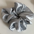 Close-up of silver-grey satin scrunchie showing glossy fabric texture and pleated details - Blue
