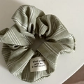 Détail du chouchou rayé vert sauge avec étiquette slogan et texture du tissu - Chouchou Rayé Vert Et Blanc