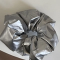 Detail eines silbernen Metallic-Scrunchies mit glänzend beschichtetem Stoff und Falten - Glänzendes Haargummi / Silber