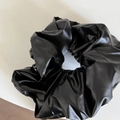 Detailansicht eines schwarzen PU-Leder Scrunchies mit sanftem Glanz und Faltenwurf - Glänzendes Haargummi / Schwarz