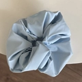 Minimalistisches hellblaues Kunstleder-Scrunchie mit Puff-Textur auf weißem Grund - Glänzendes Haargummi / Blau