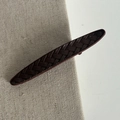 Detailed view of the dark brown braided leather hair clip on a textured fabric surface - Burgundy Striped Long Oval Clip