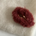Gros plan détaillé d'une pince à cheveux en peluche rouge foncé sur tricot beige - Bordeaux