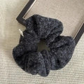 Dettaglio macro dell'elastico in lana tweed grigio scuro con consistenza morbida e etichetta - Scrunchie / Scrunchie Peloso Nero