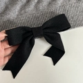 Close-up of a black knit ribbon bow detail on the ribbed hem of a gray fabric hair clip - Black