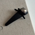 Detail of a black leather bow hair clip with a metallic grey pearl on textured fabric - Black PU Triangle Style (Pearl Bow)
