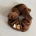 Detailed view of a soft brown pleated scrunchie featuring a wooden button and textile label - Caramel Button Hair Tie