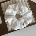 Detalle de coletero de tela blanca con dije de lazo plateado en bandeja de joyas - Coletero con lazo plateado / Blanco