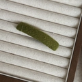 Close-up of moss green herringbone fabric hair clip on a beige linen display tray - Green Rectangular Clip