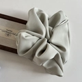 Detail of light sage green fabric scrunchie with soft pleated texture on white backdrop - Green