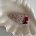 Detail einer lilafarbenen Strick-Haarspange mit bestickter roter Blume und grünem Blatt - Rosa