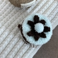 Close-up of a blue plush flower hair clip with a stylish fabric label on cozy knitwear - Cyan Coffee Cup Design