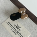 Detailed close-up of handmade acetate bow hair clip with gold lettering on beige fabric - Coffee Bow Black Hair Clip