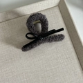 Detail of dark grey faux fur shark clip with leather bow on a beige textured tray - Small / Gray