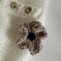 Detailaufnahme der handgestrickten Blume und braunen Harzknöpfe am weißen Haarclip - Reisrosa