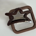Détail d'une pince à cheveux étoile marron foncé avec accents dorés sur plateau en bois - Style Creux de Pentagramme