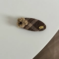 Dettaglio di un fermaglio in tessuto a scacchi marroni con fiore in maglia e tag 'Love' - Fermaglio Ovale a Righe Cachi