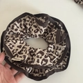 Detail view of a leopard print scrunchie with dark brown piping and a textile brand tag - White Grey Leopard Style
