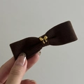 Detalle de pinza para el pelo en pana marrón con lazo y hebilla de metal dorado - Lazo Caqui