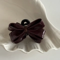 Macro di una mini clip per capelli in pelle verniciata bordeaux su vassoio bianco - Stile con fiocco rosso