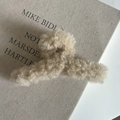 Gros plan d'une pince à cheveux en peluche beige sur un fond en tissu texturé - Blanc Cassé