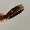 Detail eines dunkelbraunen Tweed-Haarreifens mit Metallschild und Handarbeits-Etikett - Khaki