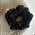 Detailopname van de zwarte geplooide satijnen scrunchie met een klein merklabel - Zwart