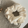 Detailopname van een geplooide beige satijnen haarelastiek met zachte ruches textuur - Broken Wit