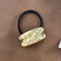 Detalle de goma de pelo con adorno cilíndrico de metal dorado y textura martillada única - Textura Cuadrada Dorada