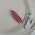 Makro-Detail einer rot-weiß karierten Tropfen-Haarklammer auf einer Keramikschale - Rot Weiß Gingham Wassertropfen Stil