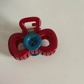 Macro detail of red bow hair claw clip with a blue button accent and golden metal spring - Red