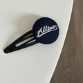Detail view of navy blue fabric button hair clip with white Alline embroidery on metal base - 10# Blue Round Accessory Clip