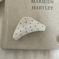 Gros plan d'une pince à cheveux beige à pois noirs sur une couverture de livre - Triangle Blanc Pois Noirs