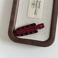 Detail van bordeauxrode gevlochten haarclip op een dienblad van linnen en hout - Rode Eendenbekclip Zwarte Streep