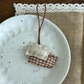 Détail d'un pendentif artisanal en tissu avec broderie sur une assiette en céramique rustique - Carré à Carreaux Caramel (9#)