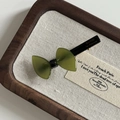Detailed macro view of dark green acetate bow hair clip with gold text on walnut wood tray - Transparent Green Bow Duckbill Clip