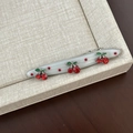 Detailed macro of a resin cherry hair clip with red rhinestones on a linen tray - White Red Polka Dot Curved Red Cherry