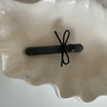 Dettaglio fermaglio per capelli in tessuto grigio con fiocco nero e logo su vassoio - Grigio Becco d'Anatra Lungo (Fiocco Nero)