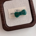 Detalle de pinza de pelo con lazo verde y texto dorado en bandeja de madera retro - verde oscuro