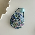 Close-up of blue floral fabric rose hair tie with a light blue bead on a cream surface - With Blue Bead Hair Tie / White with Blue Flowers