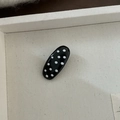 Détail d'une barrette ovale noire à pois blancs sur un plateau texturé - Pince Ovale Noire à Pois Blancs