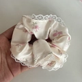 Gros plan d'un chouchou en satin fleuri avec motifs roses et bordure en dentelle - Crème avec dentelle blanche