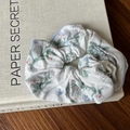 Haargummi mit Blumenmuster in Cremeweiß mit blau-roten Blüten auf einem Buch - Blaues Floral Scrunchie Blauer Rand
