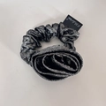 Dettaglio dell'elastico per capelli a fiore in tessuto metallico grigio con logo - Nero