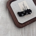 Detailed view of black denim hair clip with frayed edges and silver sequins on wooden tray - Black Denim Wave Clip